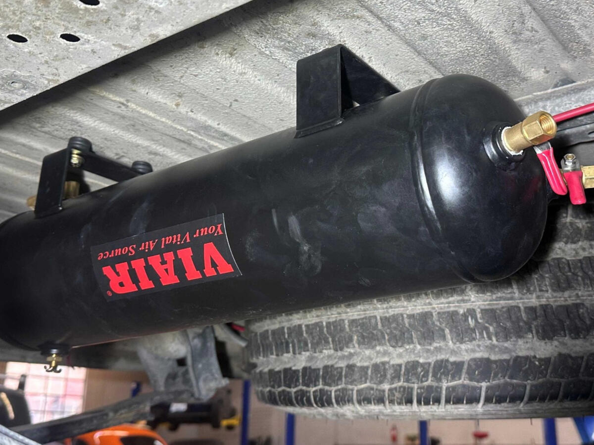 Underbody-mounted VIAIR 2.5-gallon compressed air tank installed on a Ram ProMaster camper van for rear air suspension adjustment.